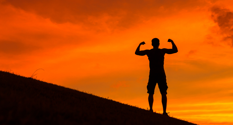 man's silhouette flexing his muscles on top of a hill with an orange sunset