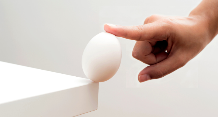 finger balancing an egg on the corner of a table
